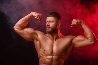 Young bodybuilder with muscular body in smoke on color background