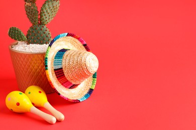 Photo of Mexican sombrero hat, cactus and maracas on red background. Space for text