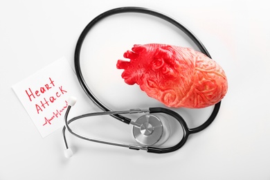 Photo of Stethoscope, note with phrase "HEART ATTACK" and model of heart on light background