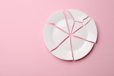 Photo of Pieces of broken ceramic plate on pink background, flat lay. Space for text