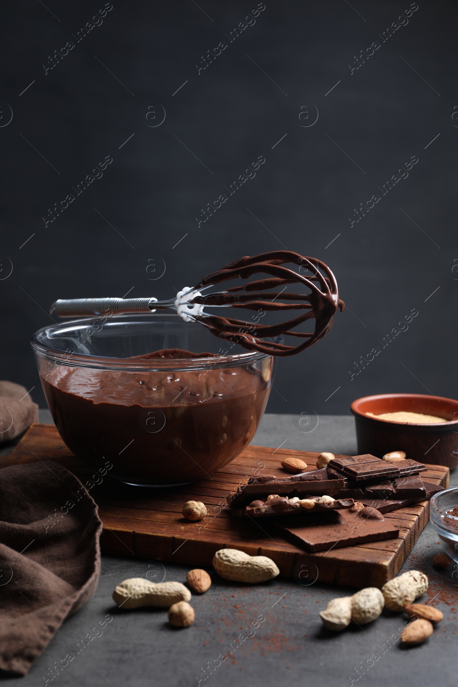 Photo of Bowl of chocolate cream, whisk and ingredients on gray table against dark background, space for text