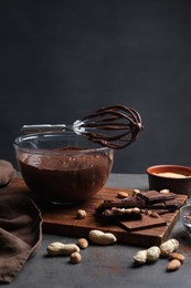 Bowl of chocolate cream, whisk and ingredients on gray table against dark background, space for text
