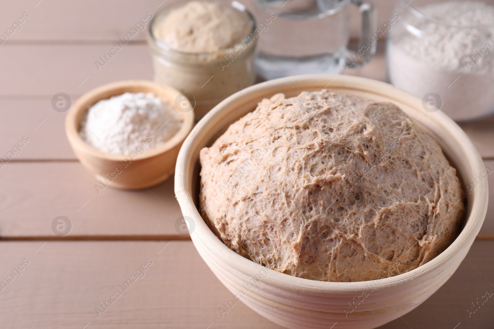 Photo of Fresh sourdough in proofing basket on wooden table, closeup