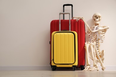 Waiting concept. Human skeleton with suitcases near light grey wall, space for text