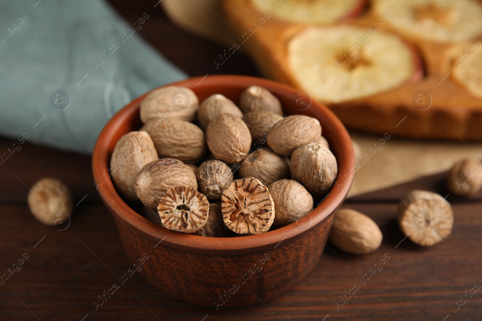 Photo of Nutmeg seeds and tasty apple pie on wooden table, closeup