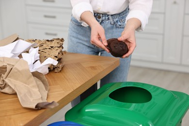 Photo of Garbage sorting. Woman throwing muffin liner into trash bin indoors, closeup