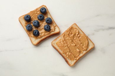 Photo of Delicious toasts with peanut butter and blueberries on white marble table, flat lay