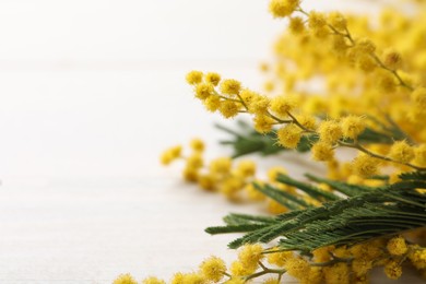 Beautiful mimosa flowers on white wooden table, closeup. Space for text