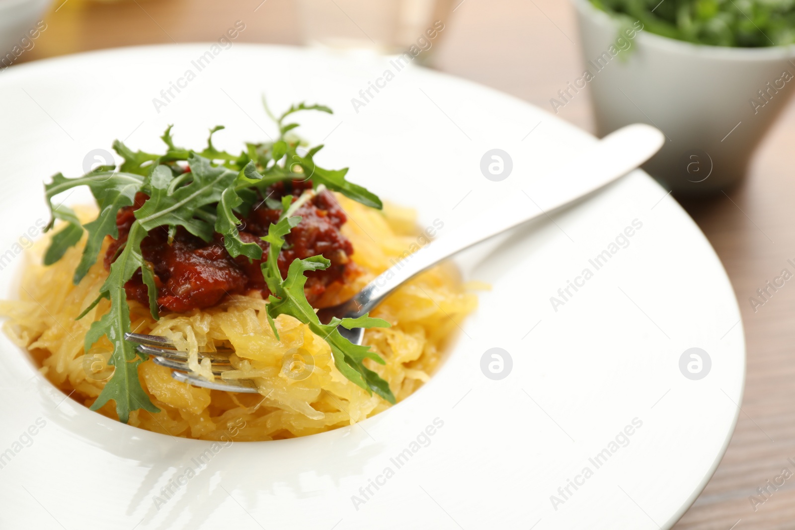 Photo of Tasty spaghetti squash with tomato sauce and arugula on table, closeup