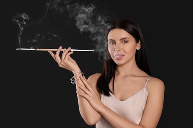 Photo of Woman using long cigarette holder for smoking on black background