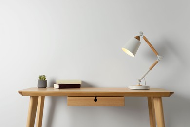 Stylish lamp, books and houseplant on wooden table near white wall. Interior design