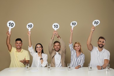 Panel of judges holding signs with highest score at table on beige background