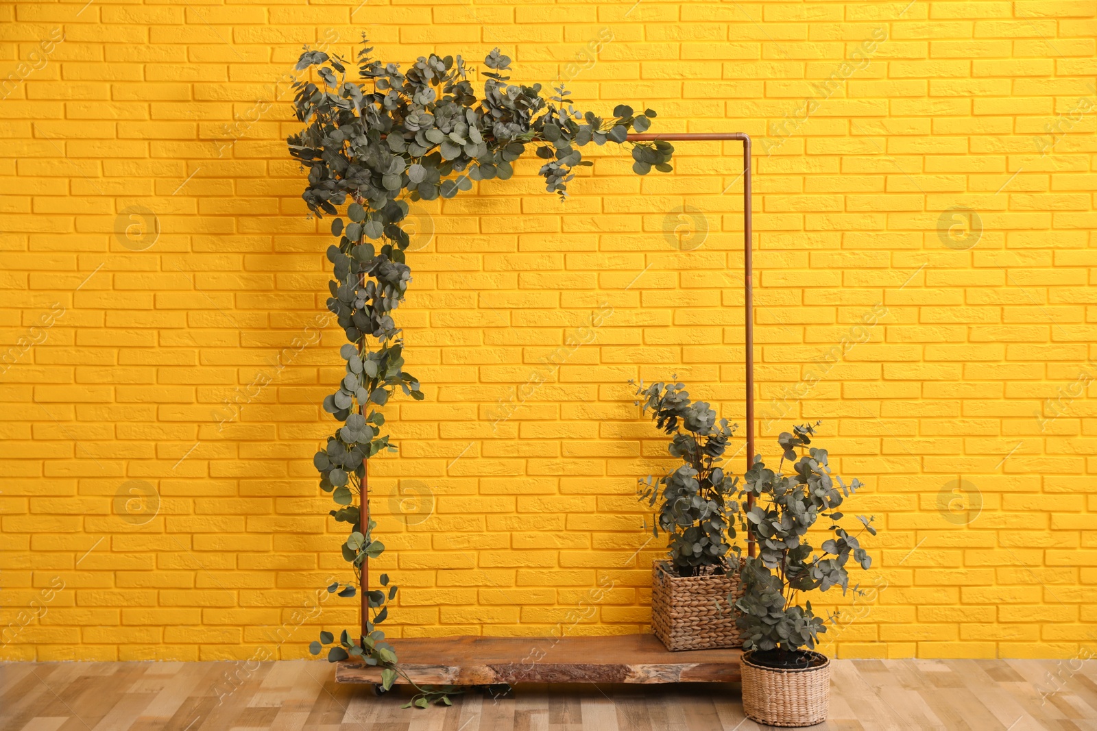 Photo of Stylish photo zone with wooden frame and green leaves near yellow brick wall indoors