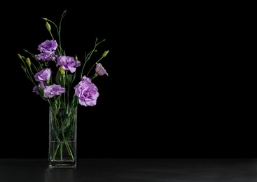 Photo of Vase with beautiful Eustoma flowers on table against dark background