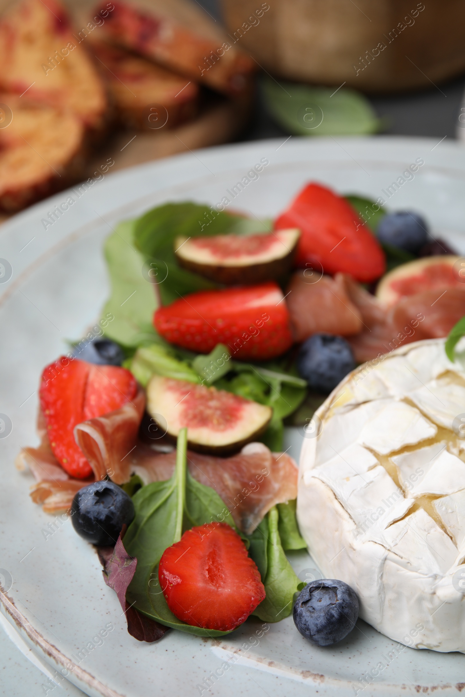 Photo of Delicious salad with brie cheese, blueberries, figs and strawberries on plate, closeup