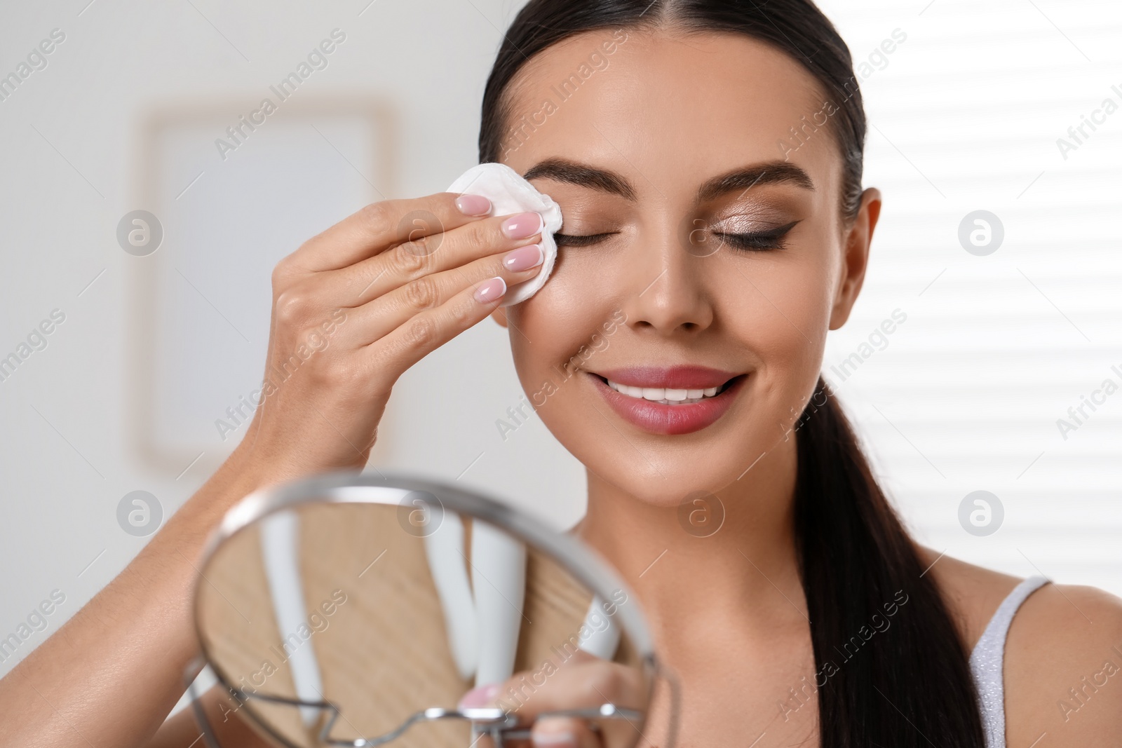 Photo of Beautiful woman removing makeup with cotton pad indoors