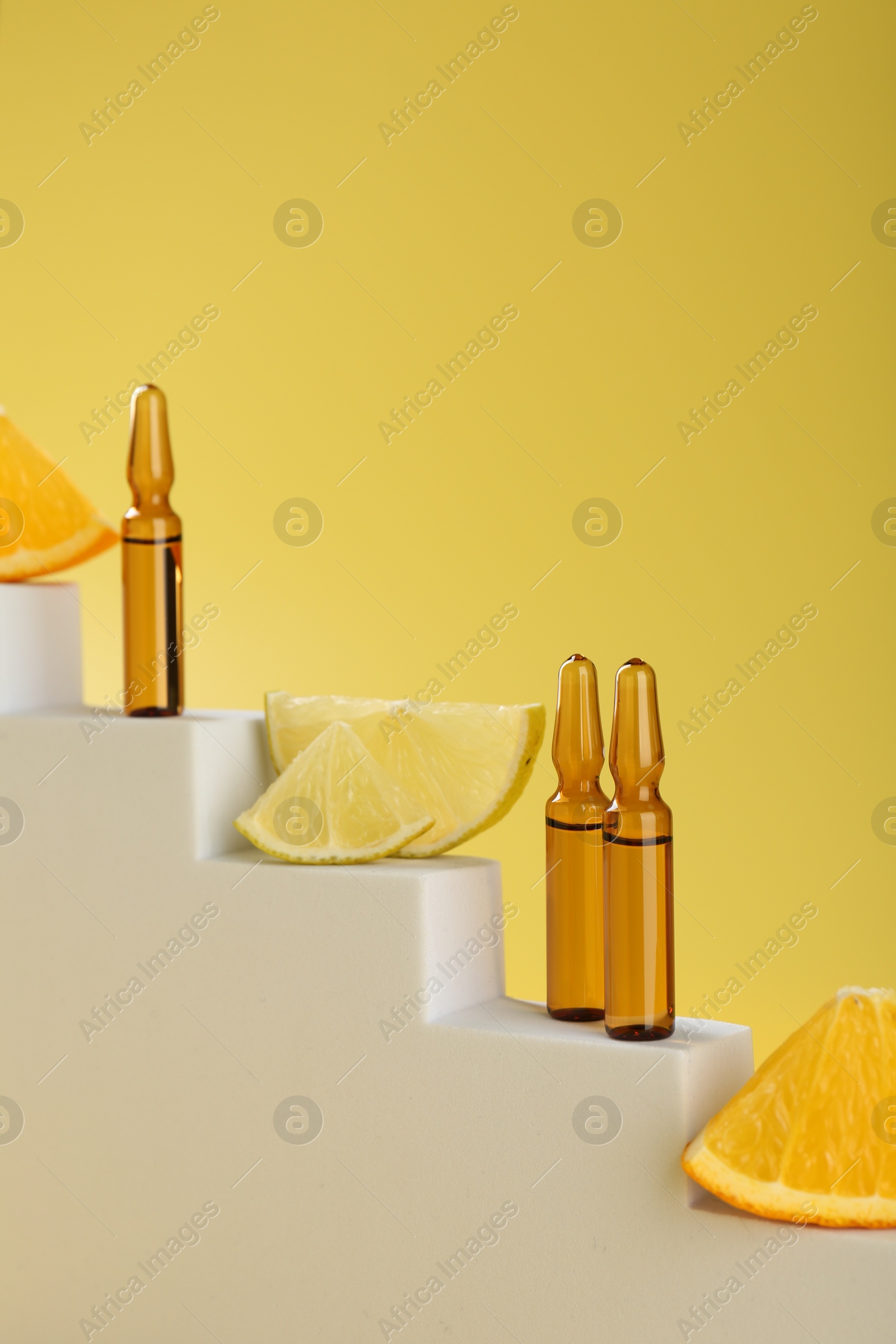 Photo of Stylish presentation of skincare ampoules with vitamin C and citrus slices on decorative stairs against yellow background, closeup. Space for text