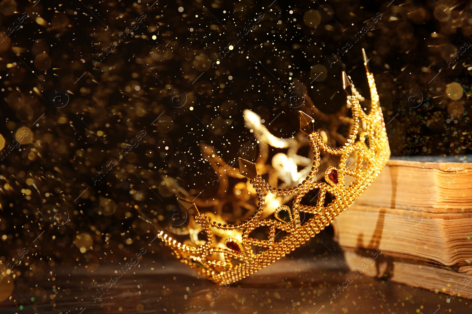 Image of Fantasy world. Beautiful golden crown and old books on table, bokeh effect