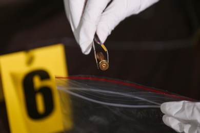 Detective putting bullet shell into plastic bag at crime scene, closeup
