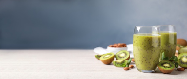 Delicious kiwi smoothie and ingredients on white wooden table. Space for text