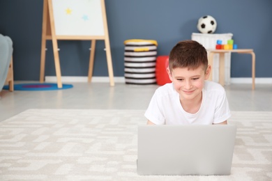 Happy boy with laptop lying on cozy carpet at home