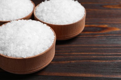 Photo of Bowls with natural sea salt on wooden table, closeup. Space for text