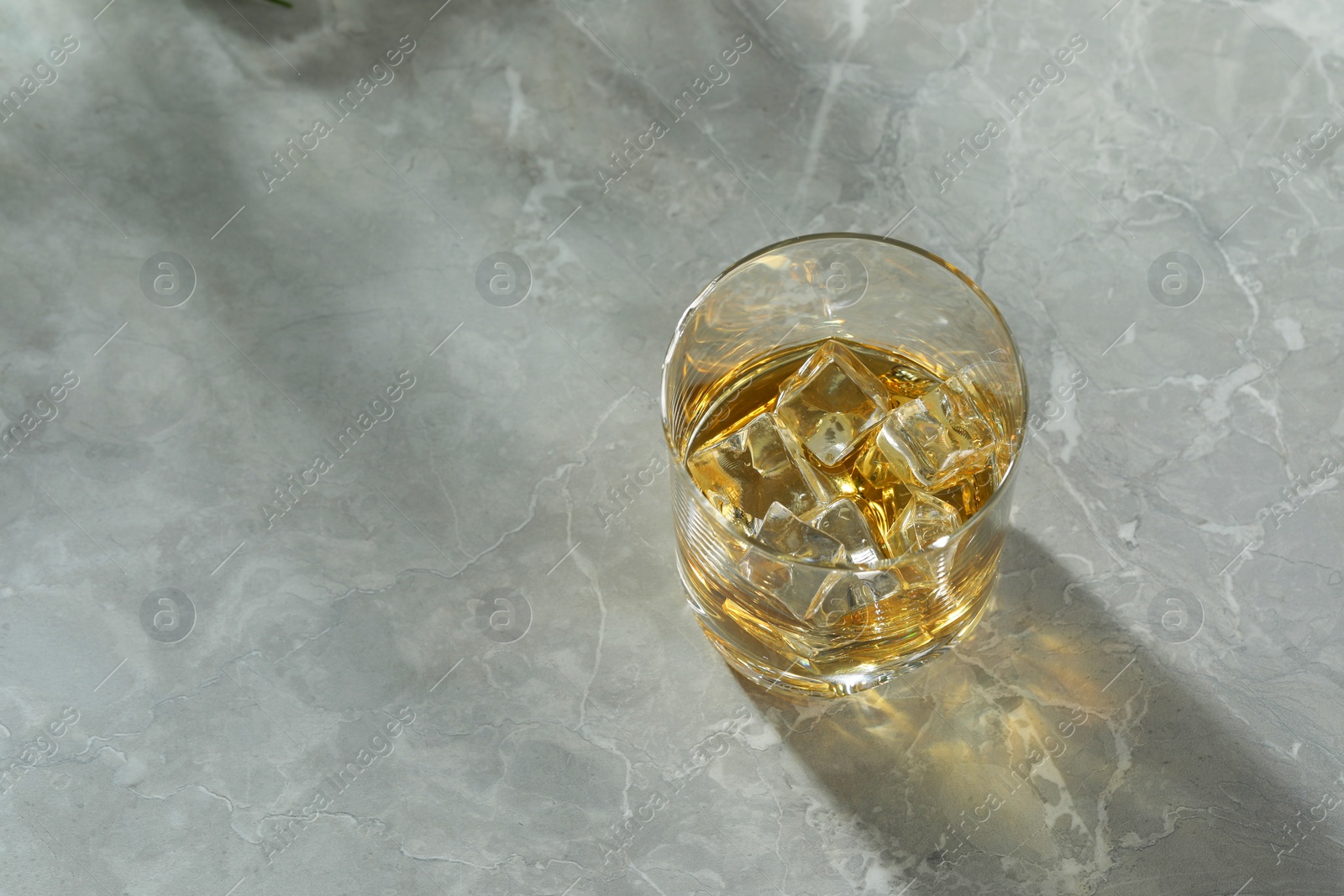 Photo of Whiskey with ice cubes in glass on grey marble table, top view. Space for text