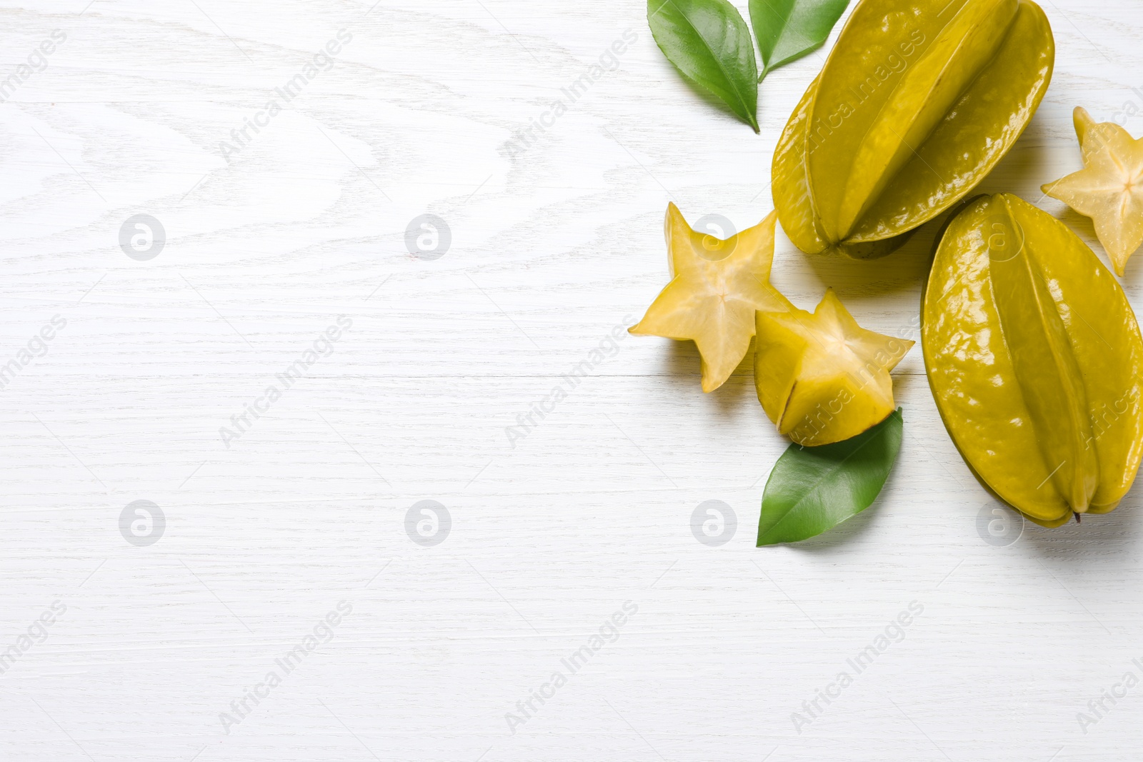 Photo of Delicious carambola fruits on white wooden table, flat lay. Space for text