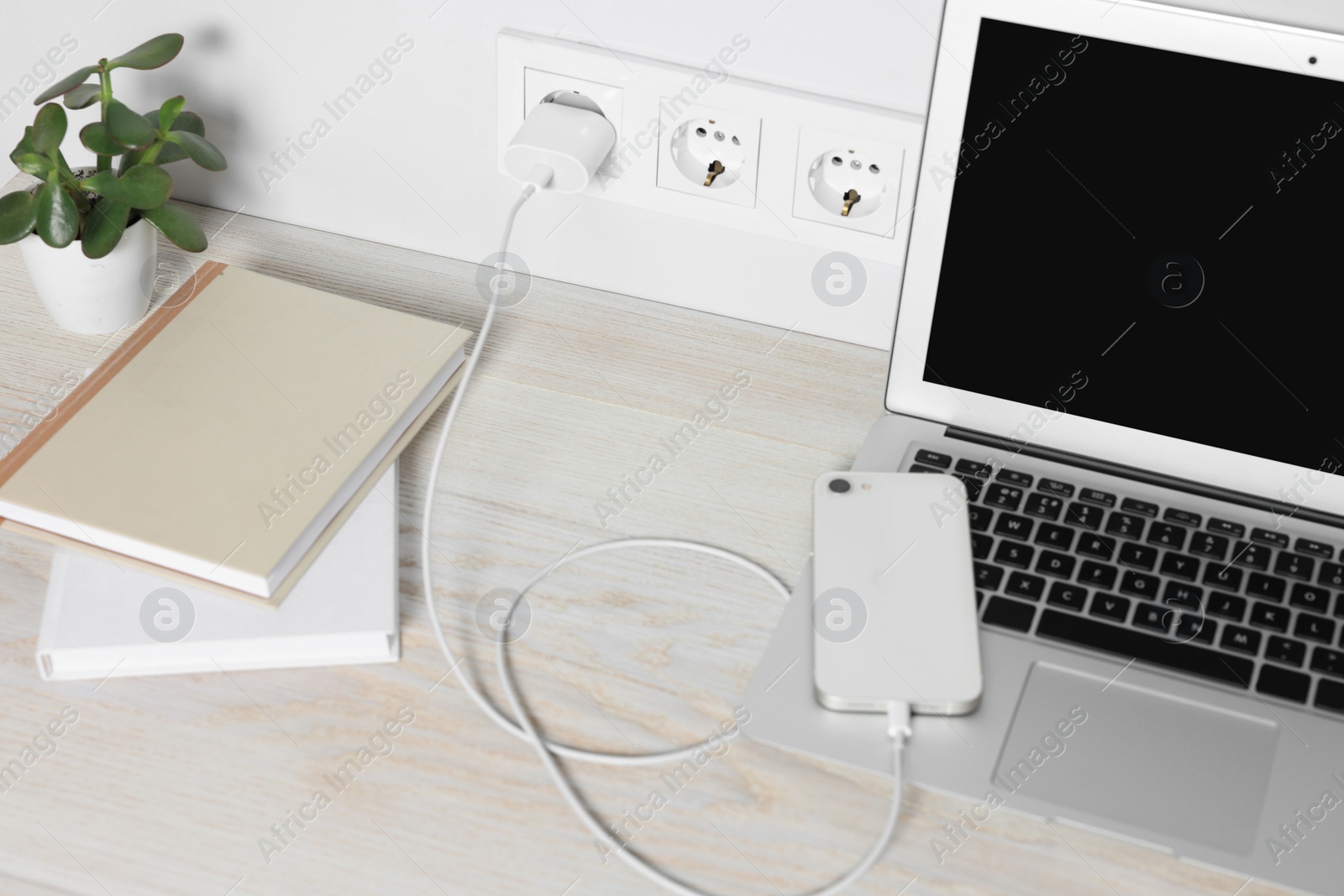 Photo of Laptop and smartphone charging on wooden table