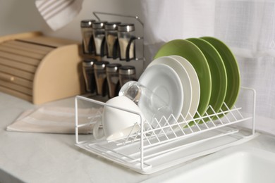 Drainer with different clean dishware, glass and cup on white table indoors