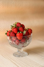 Glass dessert bowl with ripe strawberries on white wooden table