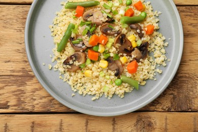 Photo of Delicious bulgur with vegetables and mushrooms on wooden table, top view