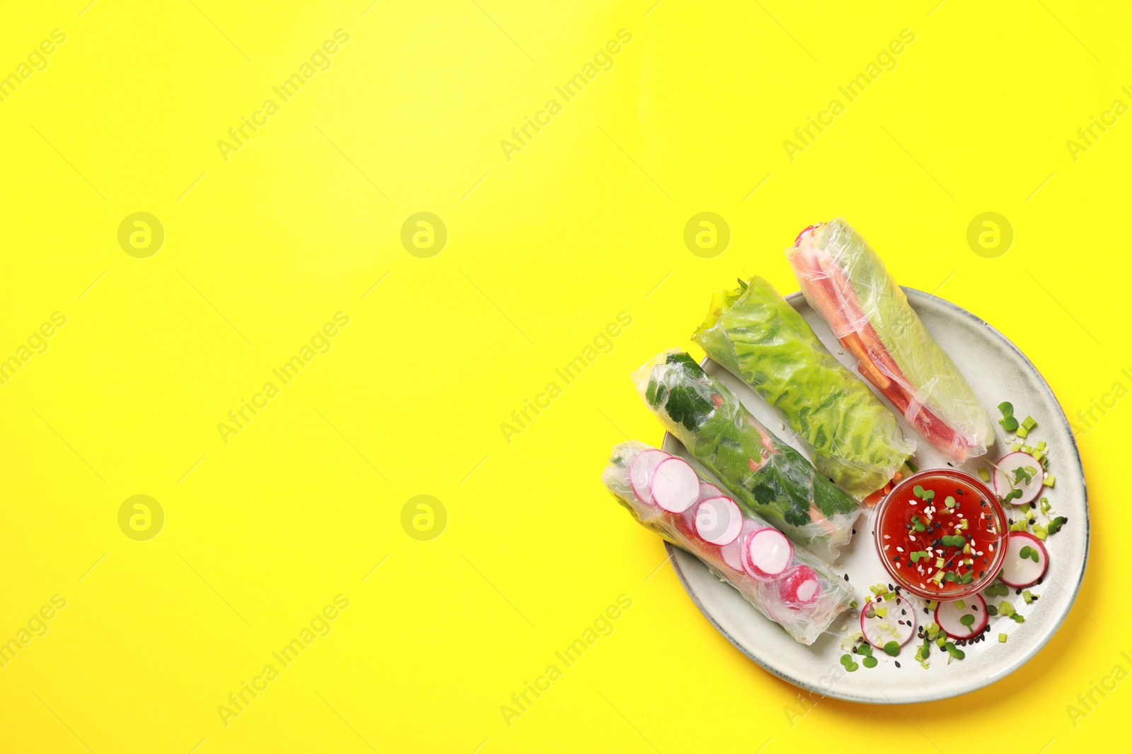 Photo of Delicious spring rolls served with sauce on yellow background, top view. Space for text