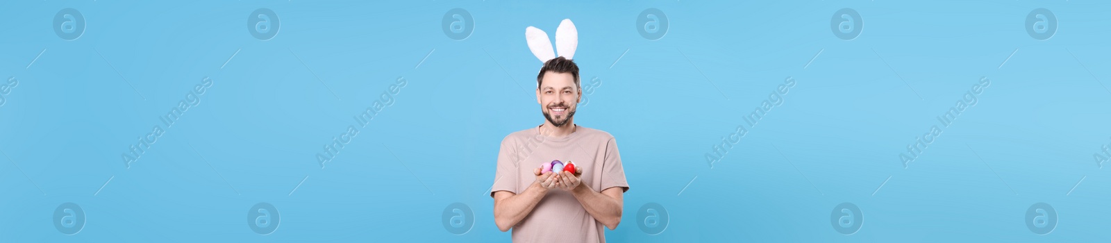 Image of Happy man with bunny ears holding Easter eggs on light blue background. Banner design