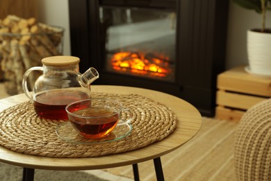 Photo of Teapot and cup of drink on coffee table near stylish fireplace in cosy living room. Interior design