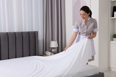 Photo of Young maid making bed in hotel room. Space for text