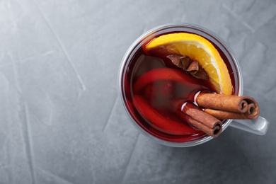 Photo of Glass cup with mulled wine on grey table, top view. Space for text