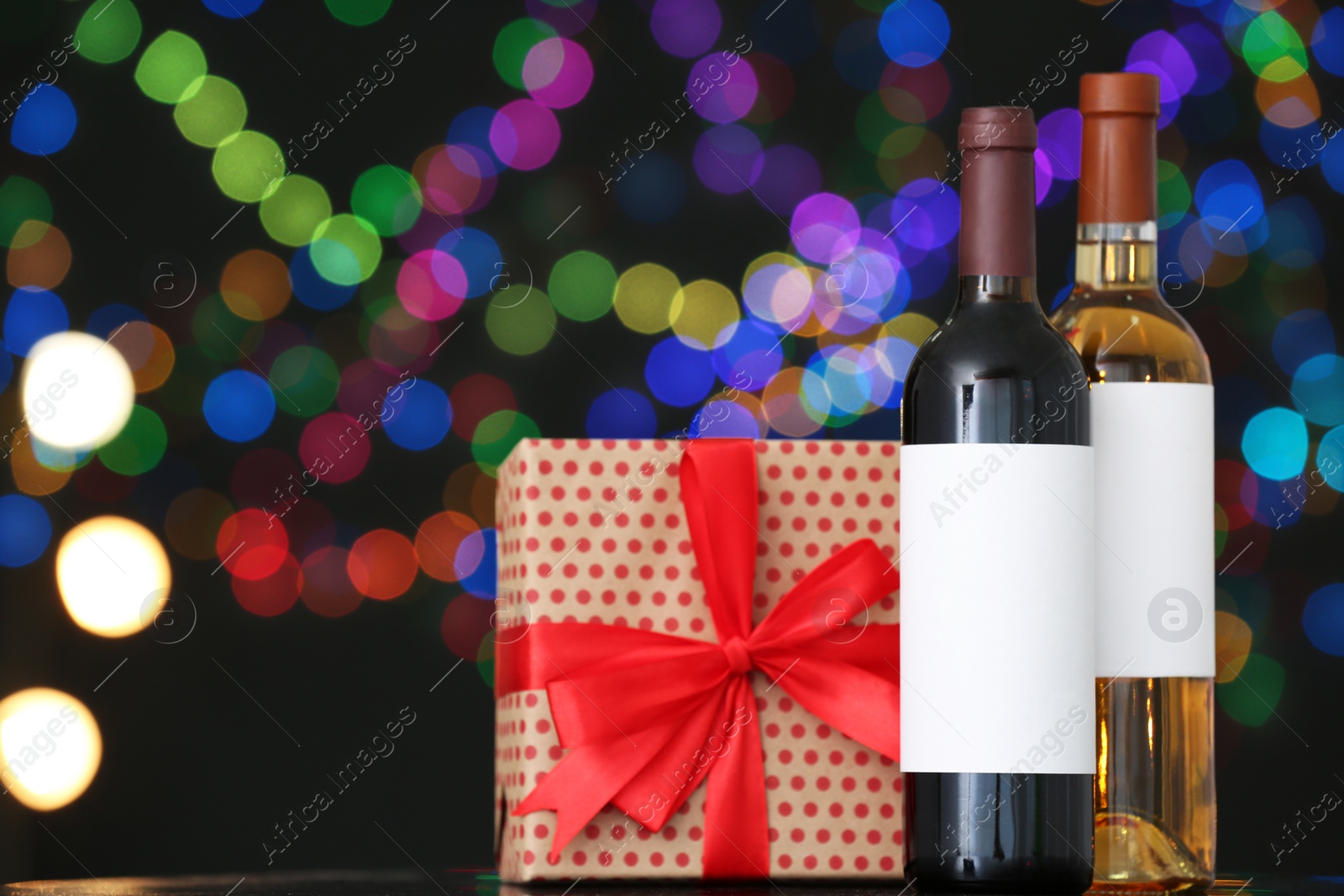 Photo of Gift box with and bottles of wine on table against blurred lights, space for text. Bokeh effect