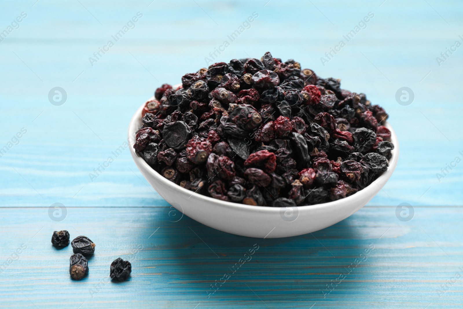 Photo of Bowl of dried black currant berries on light blue wooden table