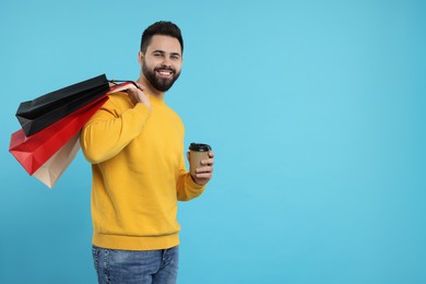 Smiling man with paper shopping bags and takeaway coffee on light blue background. Space for text