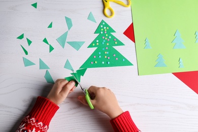 Photo of Little child making Christmas card at white wooden table, top view