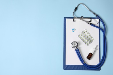 Stethoscope, pills, nasal spray and clipboard on light blue background, top view. Space for text