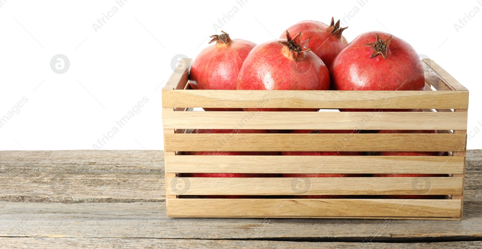 Photo of Fresh pomegranates in crate on wooden table against white background