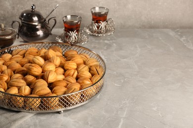 Photo of Delicious walnut shaped cookies and cups of tea on grey table, space for text. Tasty pastry carrying nostalgic home atmosphere