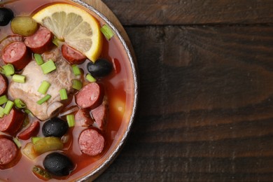 Photo of Meat solyanka soup with thin dry smoked sausages in bowl on wooden table, top view. Space for text