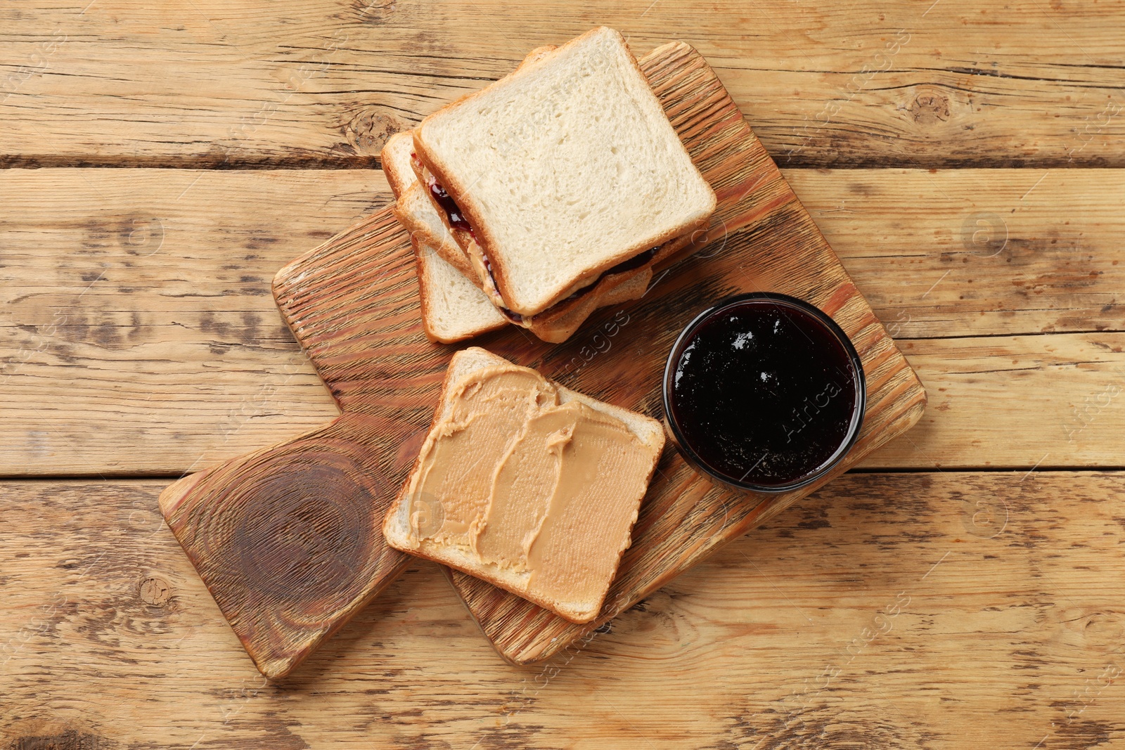 Photo of Tasty peanut butter sandwiches and jam on wooden table, top view