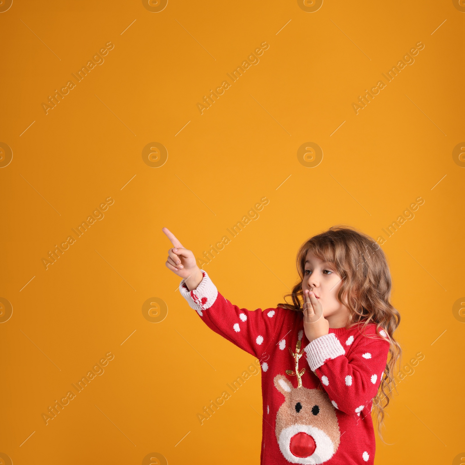 Photo of Cute little girl in red Christmas sweater against orange background. Space for text