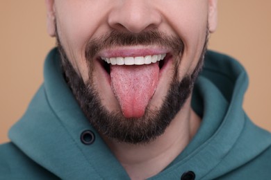 Happy man showing his tongue on beige background, closeup