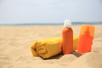 Photo of Sunscreens and rolled towel on sandy beach, space for text. Sun protection care
