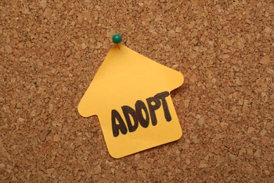 Photo of House shaped note with word ADOPT pinned to cork board